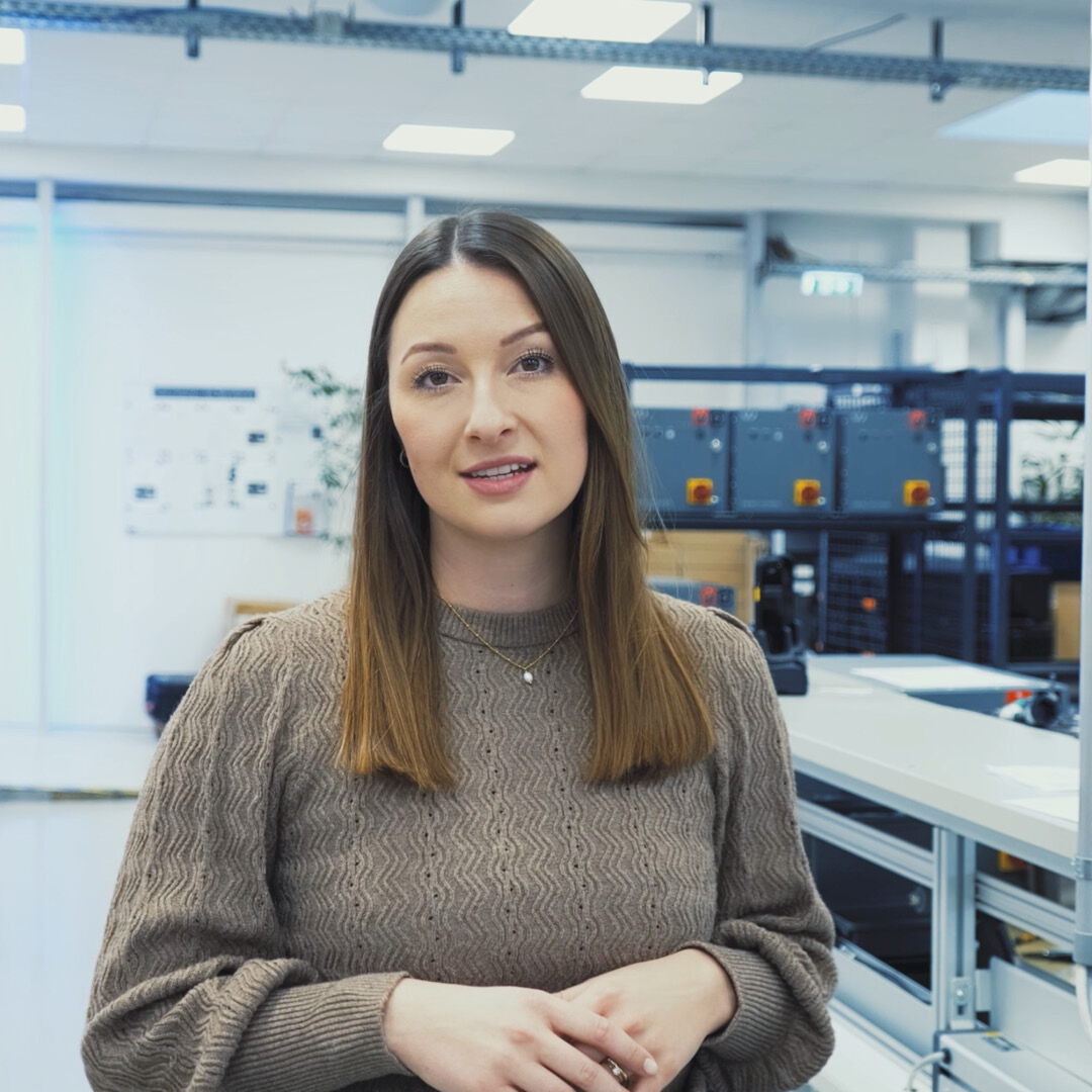 Video thumbnail on the topic of consulting: A friendly female consultant sits in a technical lab or workshop, looking towards the camera.