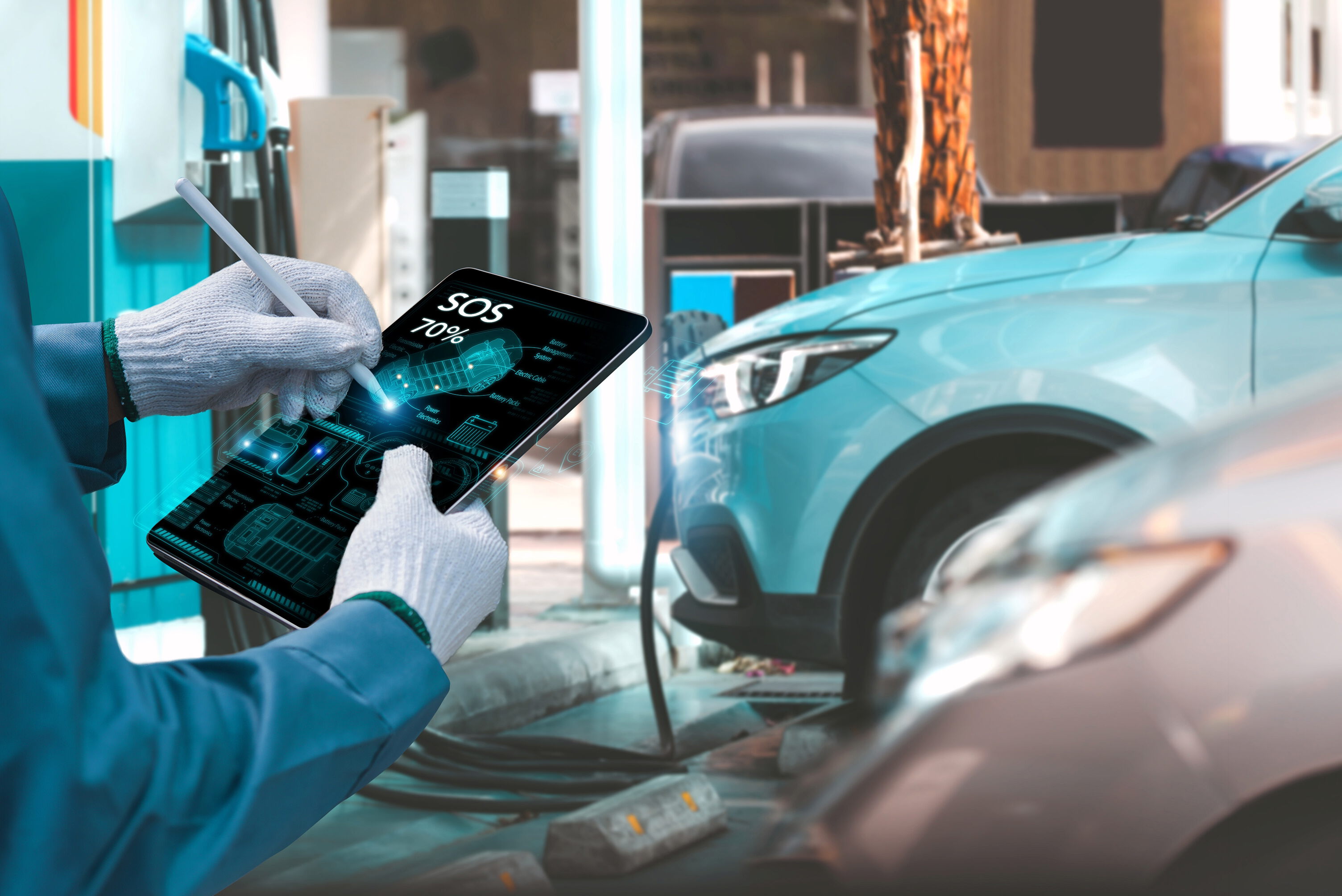 A technician wearing work gloves uses a tablet to check the SOS emergency system of a modern car, which is visible in the background of a service station.